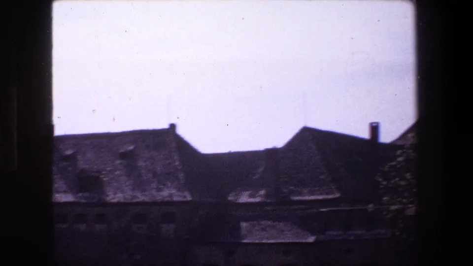 1970 Strasbourg 8mm frame showing weathered sloped-roof buildings partly obscured by dark foreground framing near a still body of water.