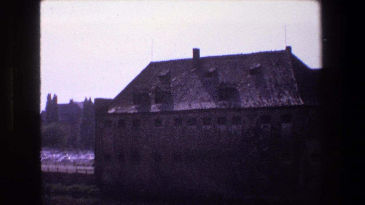 1970 Strasbourg 8mm view of a large worn masonry building with a steep roof, small windows, and water reflecting light in the background.