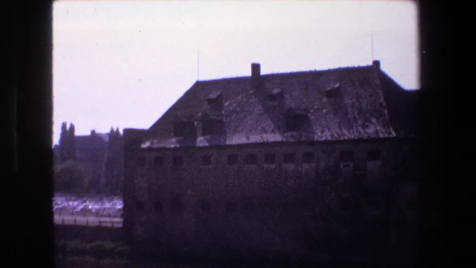 1970 Strasbourg 8mm view of a large worn masonry building with a steep roof, small windows, and water reflecting light in the background.