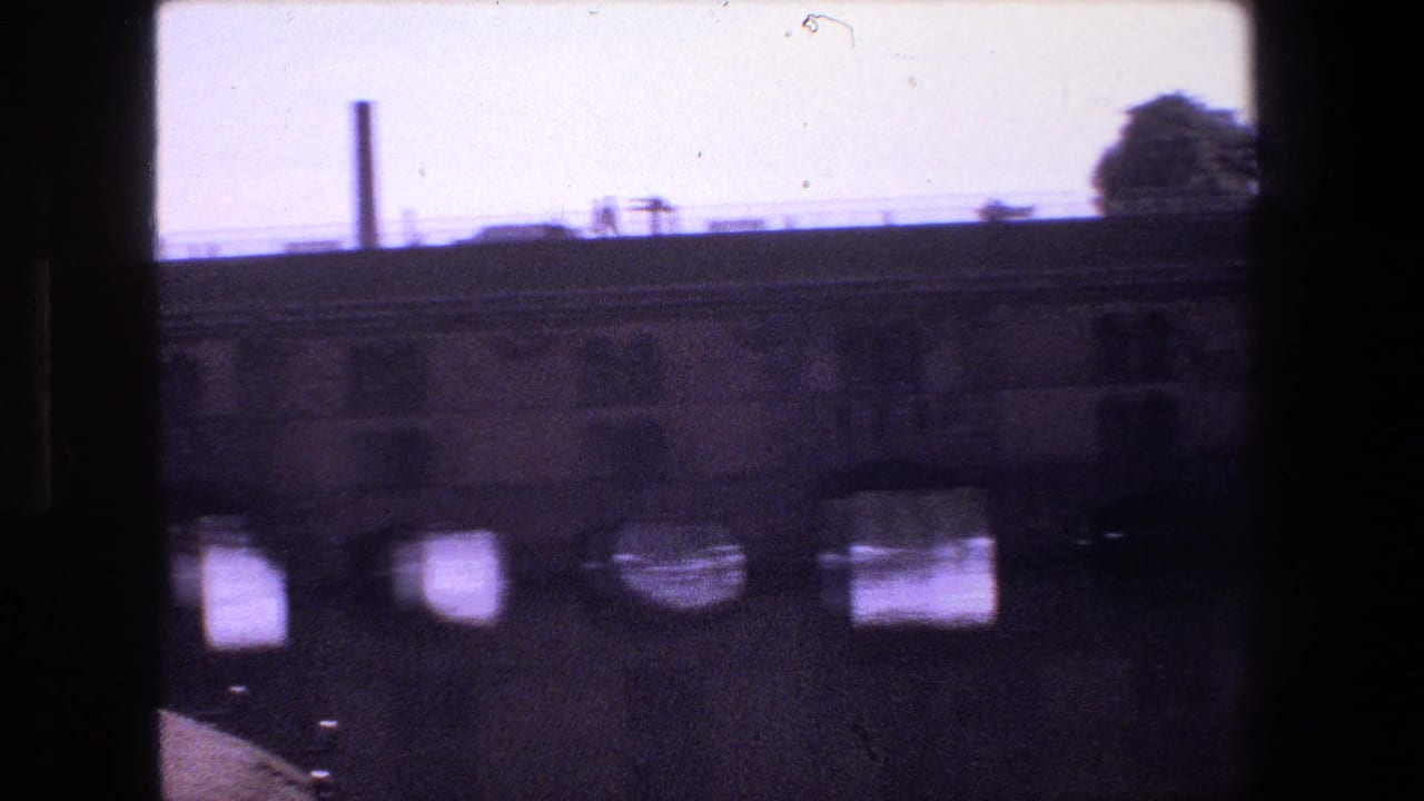Bridge arches over water with a tall chimney in the distance.