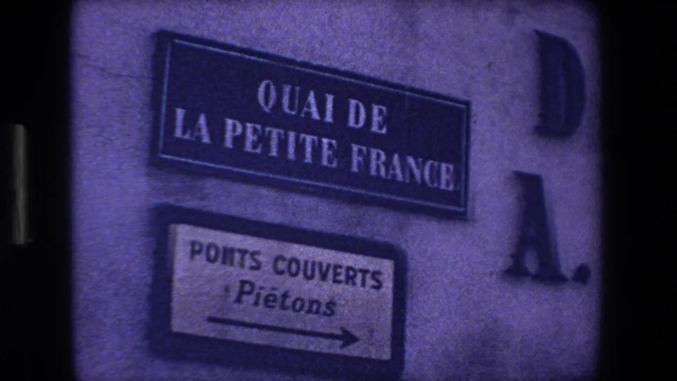 1970 8mm Strasbourg frame showing a wall-mounted Quai de la Petite France sign above a Ponts Couverts pedestrian direction sign.