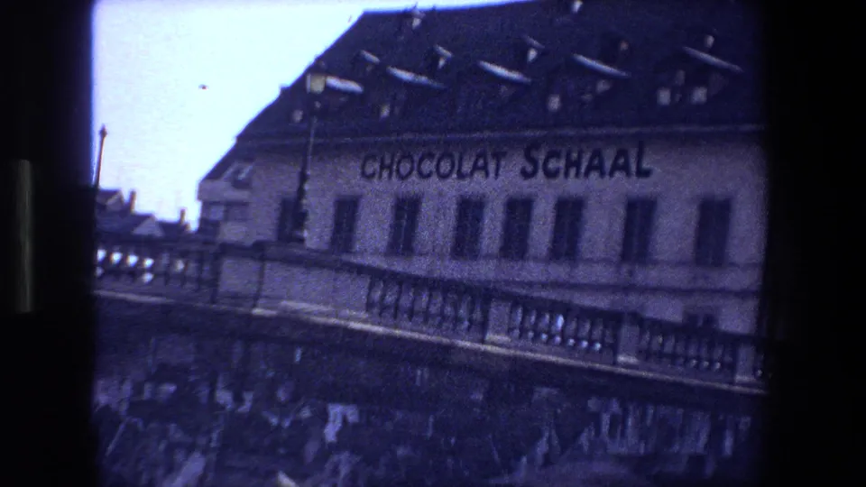 1970 8mm view in Strasbourg showing a canal-side building marked Chocolat Schaal behind stone bridge railings and dark water.