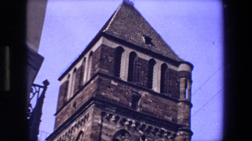 The camera tilts toward a historic stone tower in Strasbourg, with arched openings, masonry detail, bright sky, and visible 8mm frame edges.