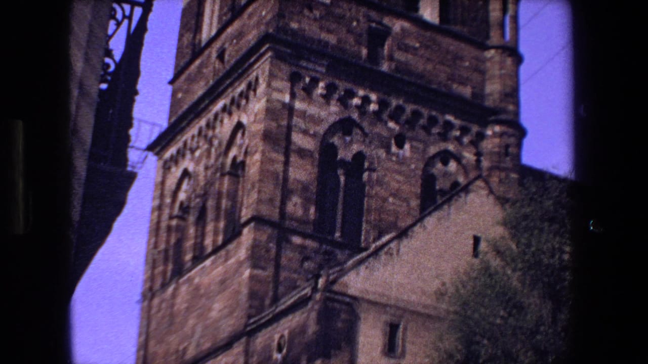 1970 8mm footage of a historic stone church exterior in Strasbourg, France, with towers, arched windows, and dark street edges framing the view.