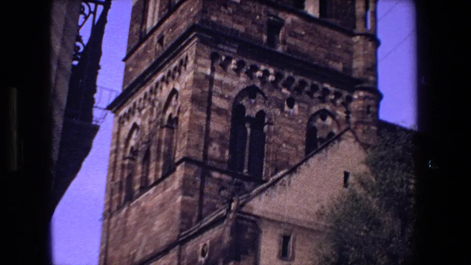 1970 8mm footage of a historic stone church exterior in Strasbourg, France, with towers, arched windows, and dark street edges framing the view.