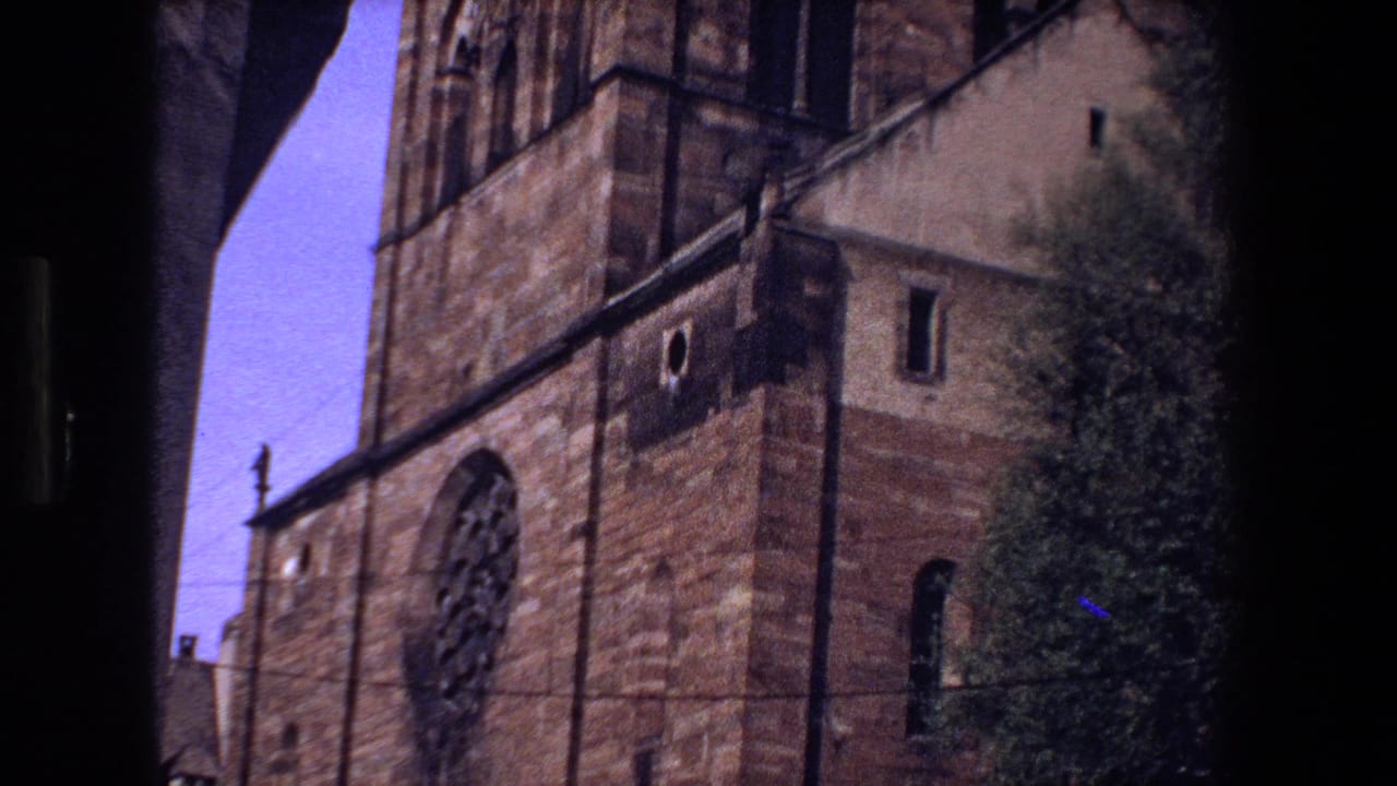 1970 visitor-shot view of a Strasbourg church facade with a prominent rose window, arched openings, stonework, and nearby greenery.