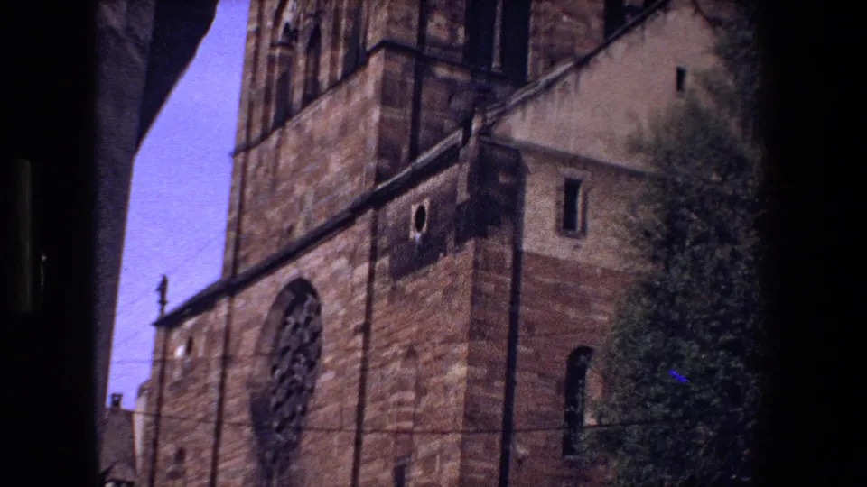 1970 visitor-shot view of a Strasbourg church facade with a prominent rose window, arched openings, stonework, and nearby greenery.