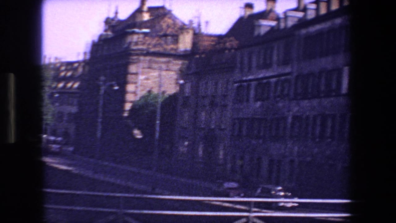 Street and bridge view with large stone buildings and traffic in shadow.