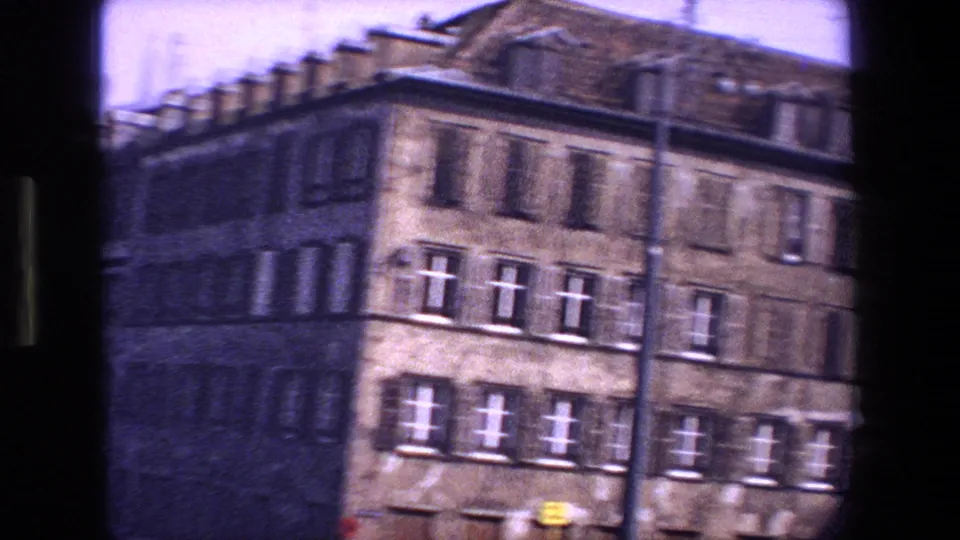 1970 Strasbourg home-movie frame showing multi-story stone apartment facades with shuttered windows, filmed quickly from a passing vehicle.