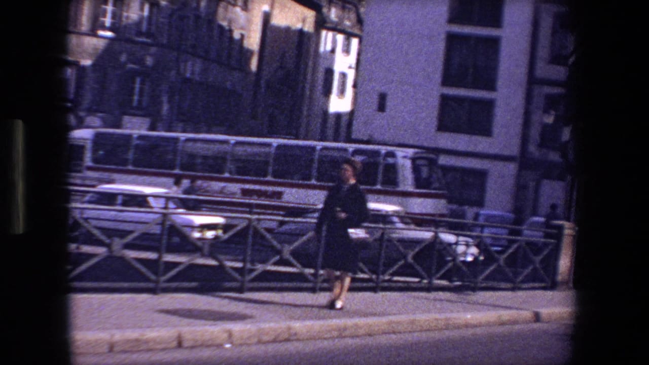 Woman walking along a city sidewalk with railings, cars, and a bus behind her.
