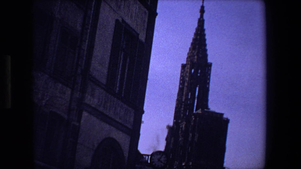 Dark cathedral spire rising beside a masonry building against a blue-purple sky.