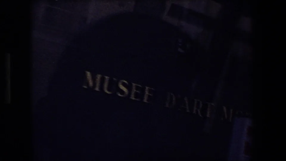 Dim 1970 Strasbourg, France frame showing a close, underexposed sign with MUSEE partly legible, likely near the cathedral area shown in the clip.