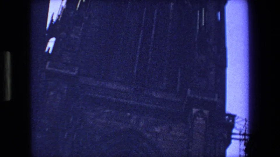 1970 Strasbourg, France 8mm frame showing a shadowed stone facade seen from below, with a narrow strip of blue sky at the edge.