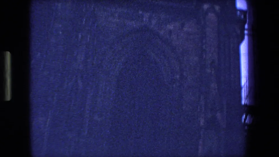 1970 Strasbourg, France 8mm frame showing dark, grainy stonework with a bright vertical blue sky strip along the right edge.