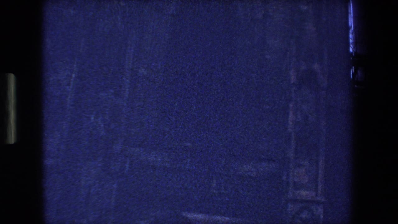 Dark, underexposed 8mm frame from the Strasbourg, France clip, showing blue film texture, gate shadows, scratches, and little discernible subject detail.