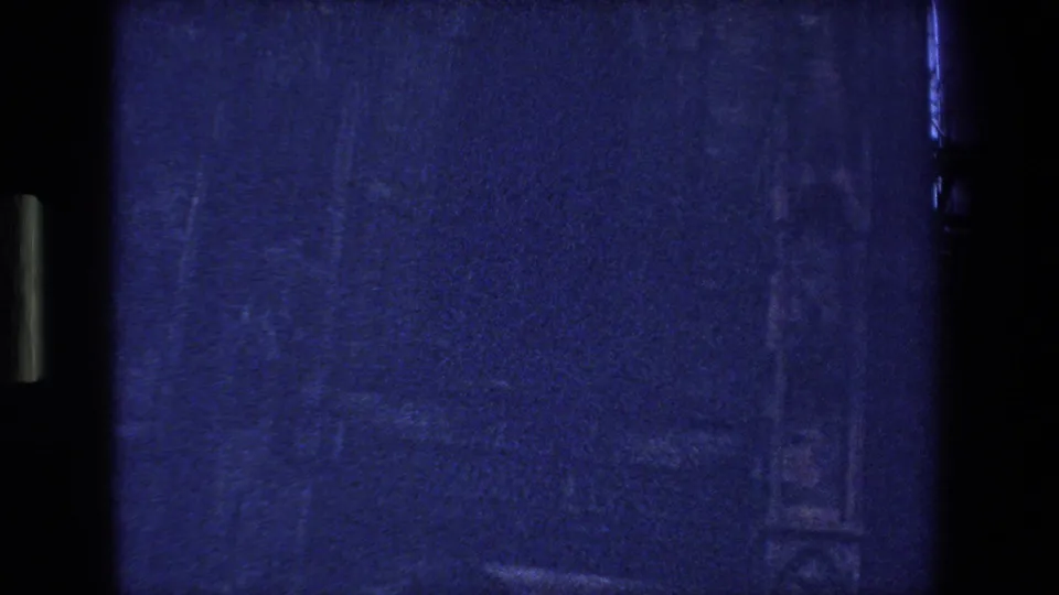 Dark, underexposed 8mm frame from the Strasbourg, France clip, showing blue film texture, gate shadows, scratches, and little discernible subject detail.