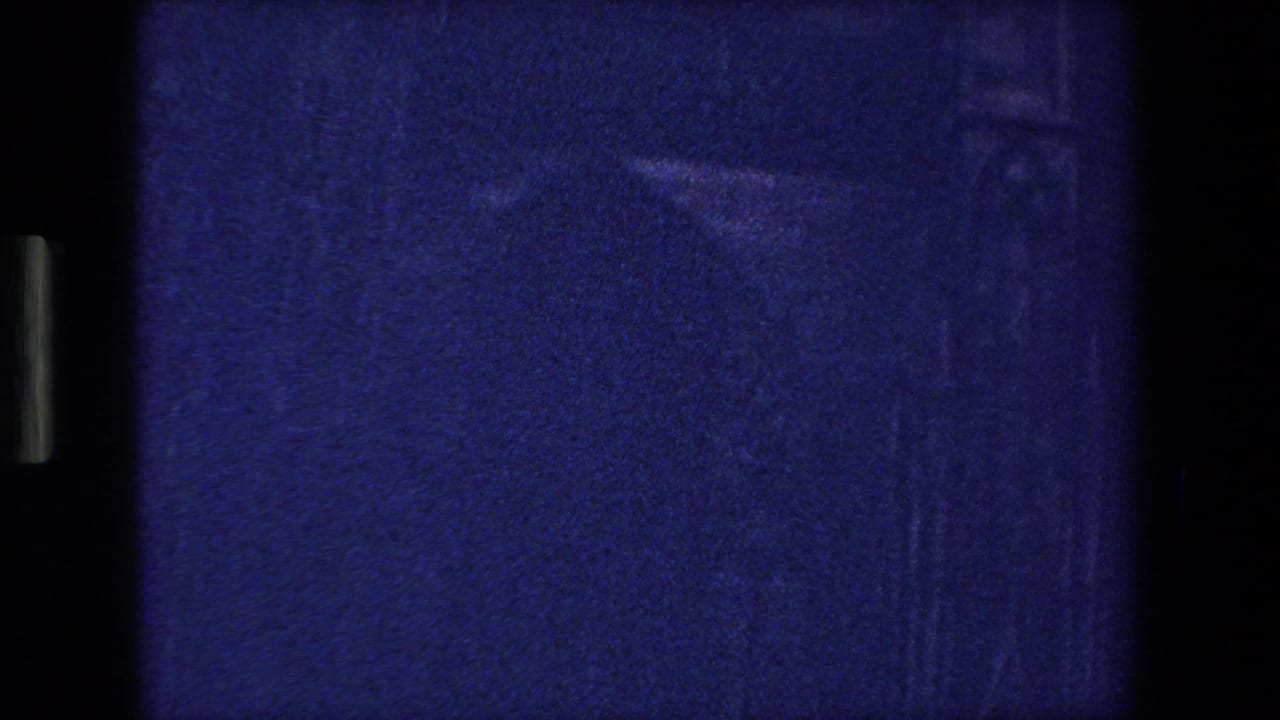 Underexposed 8mm frame from the 1970 Strasbourg footage, dominated by blue-purple grain, vertical gate shadows, and faint marks from the film scan or projection.