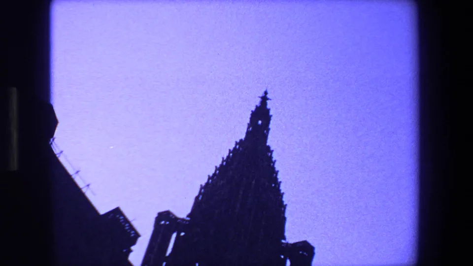 Silhouetted Gothic church spire in the supplied 1970 Strasbourg, France clip, seen through dark 8mm film borders against a purple-blue sky.