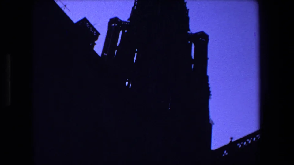 A dark Gothic cathedral mass and spire dominate the frame in this Strasbourg, France 8mm home-movie view, with blue twilight sky visible around the silhouette.