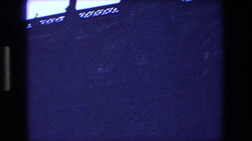 1970 Strasbourg home-movie frame showing a dark Gothic church edge and pointed spire silhouetted against a saturated blue twilight sky, with visible 8mm grain and frame-edge shadow.