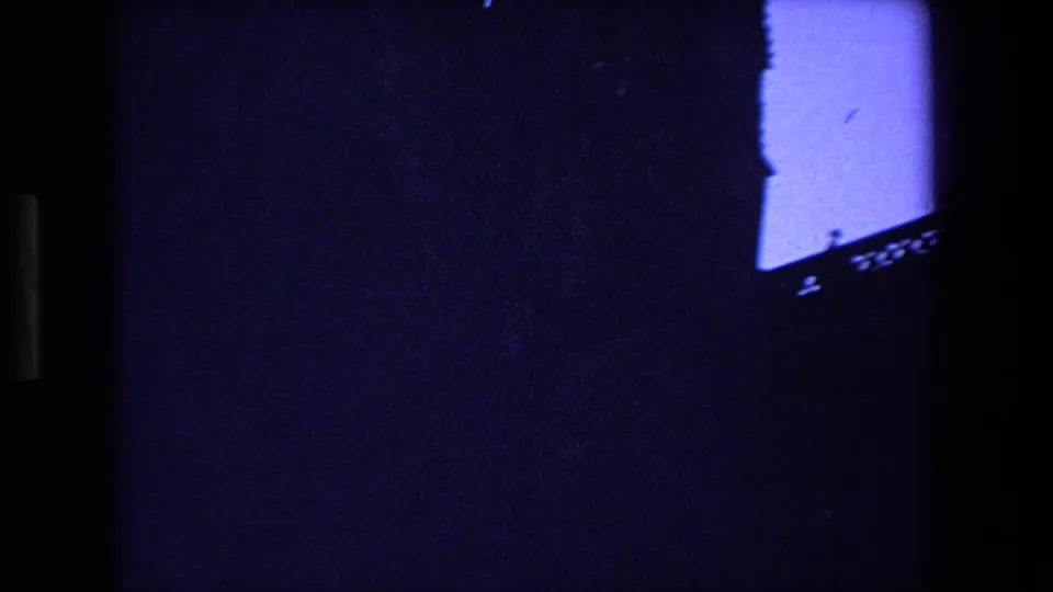 The 1970 Strasbourg footage briefly shows a partial Gothic roofline and bright blue twilight opening, with much of the frame falling into dark 8mm shadow and border area.
