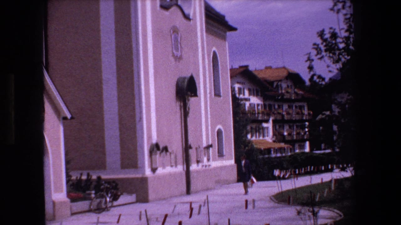 Church exterior beside a paved walkway with a pedestrian and background buildings.