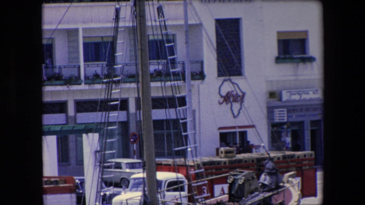 Rigging and mast obscure a white building with balconies, cars, and an Africa-shaped wall graphic.