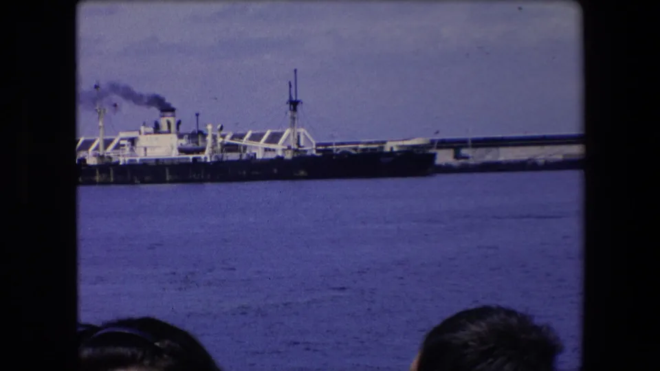 The ship remains partly visible at the left edge, smoke trailing above the pier while the harbor water fills the foreground.