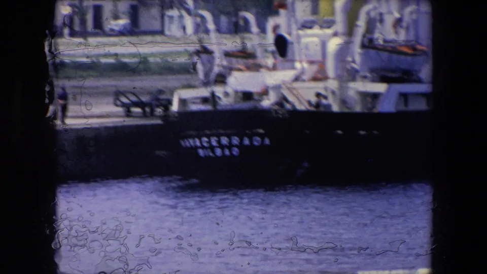 Soft 1971 8mm zoom detail of the ship stern at the waterfront, with the NAVACERRADA lettering partly visible, a person on the pier, and water in the foreground.