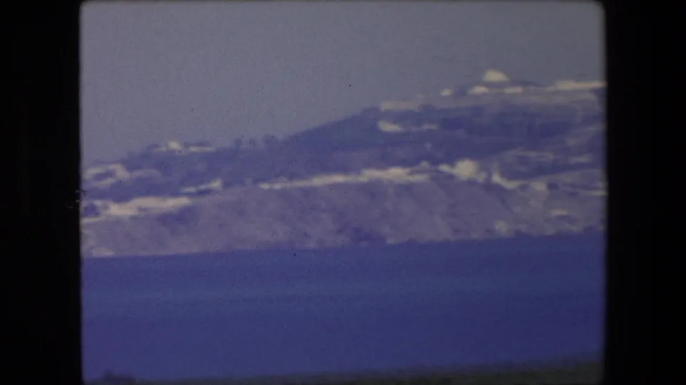 1971 Algeria home-movie frame showing a soft-focus coastal hillside with white structures and a dark strip of foreground below the sea view.