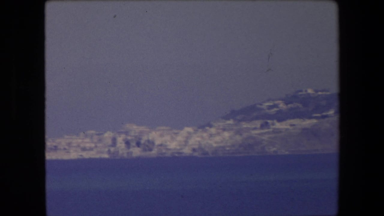 White shoreline buildings on a distant peninsula across blue water.