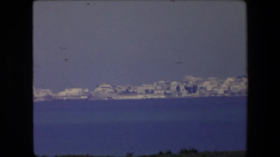 1971 Algeria 8mm frame showing a low coastal skyline and clustered pale buildings seen from across open water.