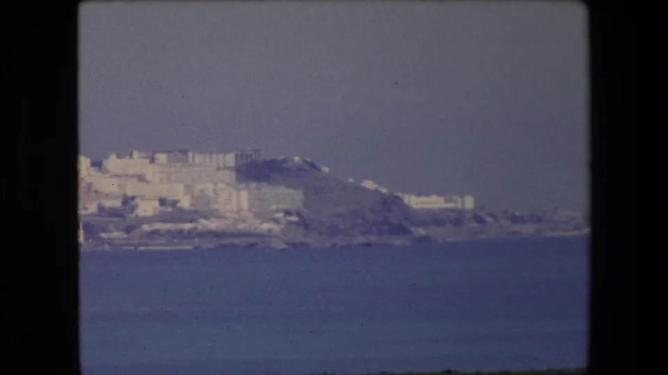 Soft 8mm frame from Algeria in 1971 showing clustered pale buildings on a coastal hillside above the blue water.