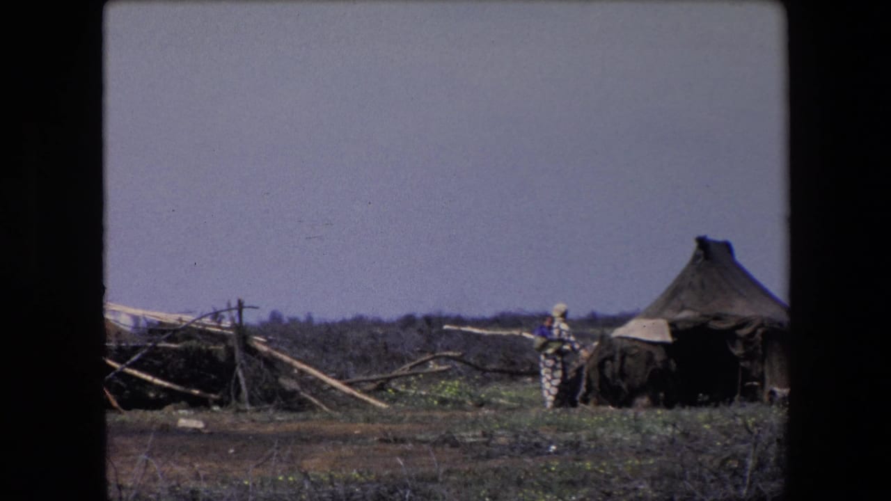 Person in patterned clothing near a dark shelter and conical hut.