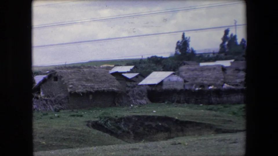 The final frame holds on a rural village landscape in Algeria, showing thatched structures, grass, a road above them, and visible home-movie exposure variation.
