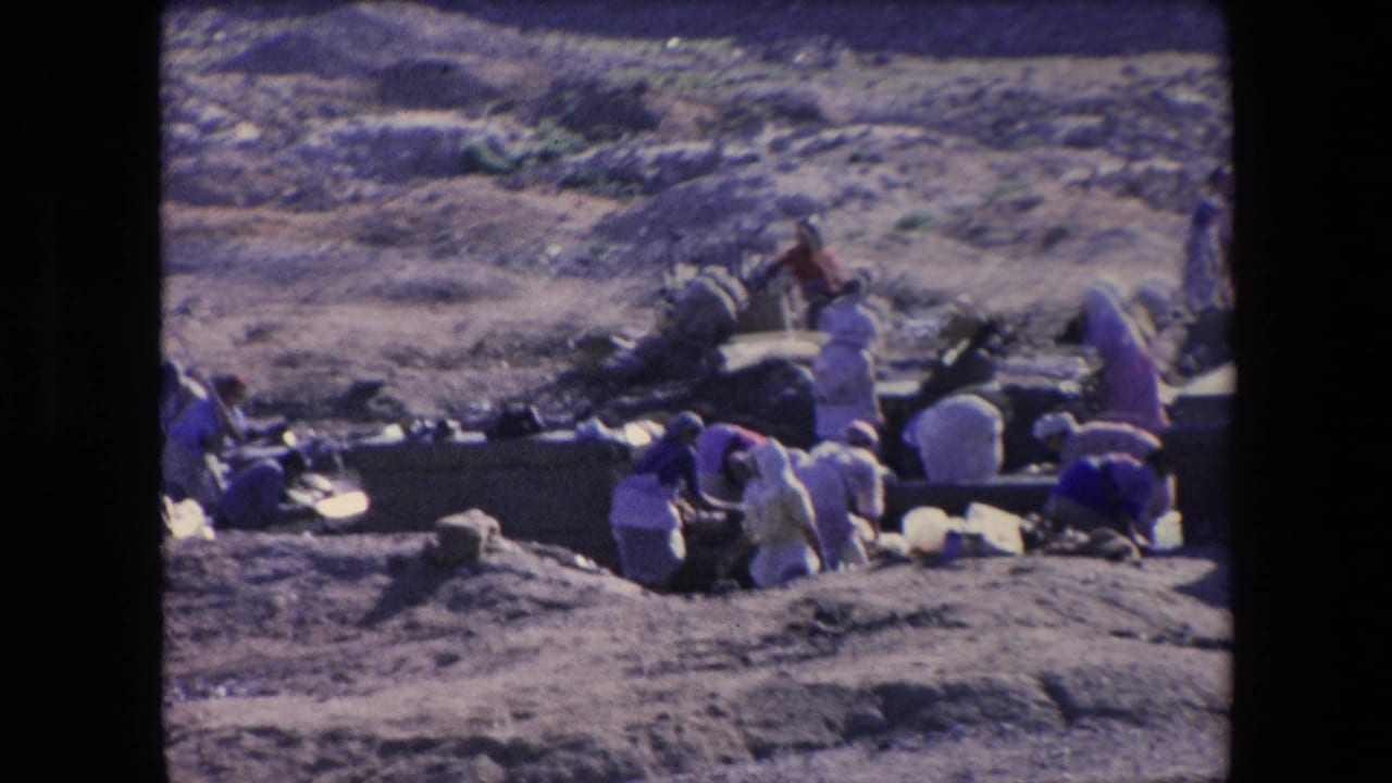 In 1971 Algeria 8mm footage, several robed figures appear to work or dig near low stone-lined ground in a dry, open field.