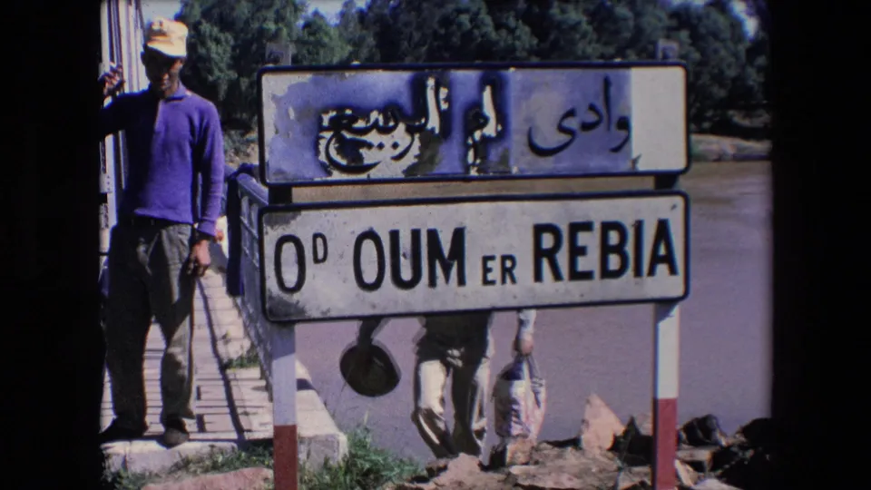 The weathered Oum Er-Rbia sign fills the frame, with Arabic script above Latin lettering and men partially visible around the bridge area.