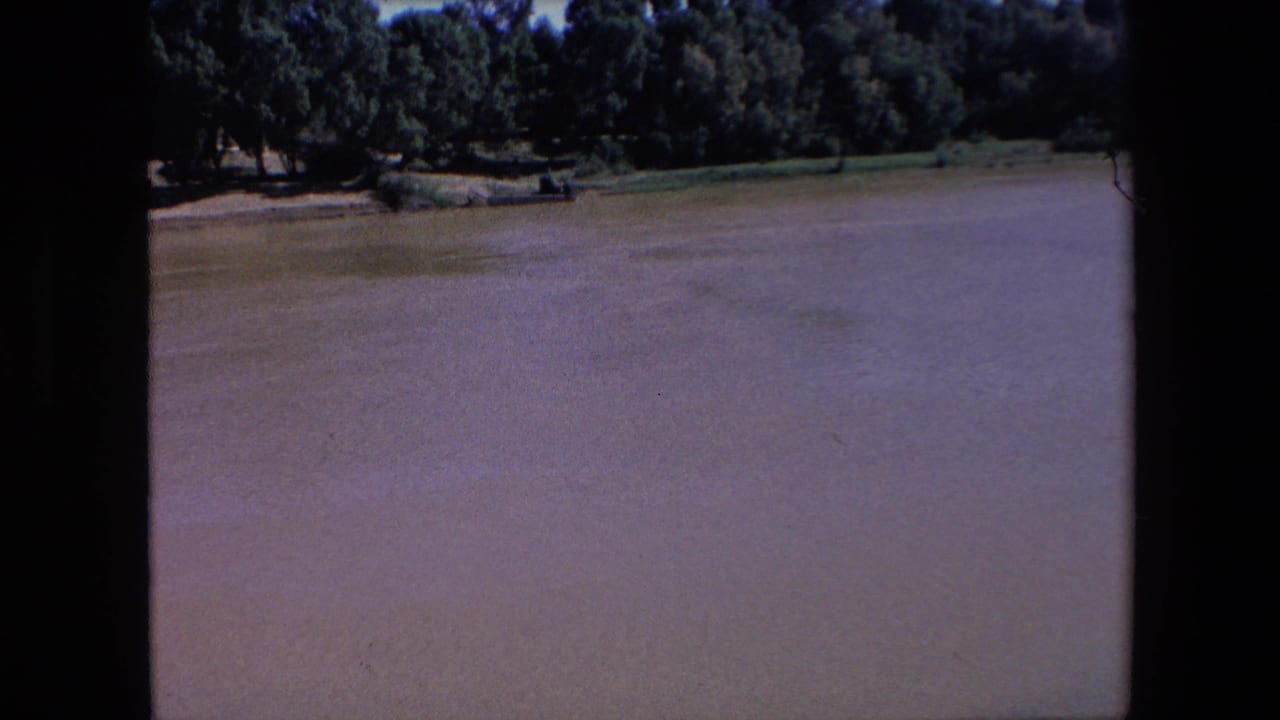 Broad muddy river with a tree-lined far bank and dark vertical film border.