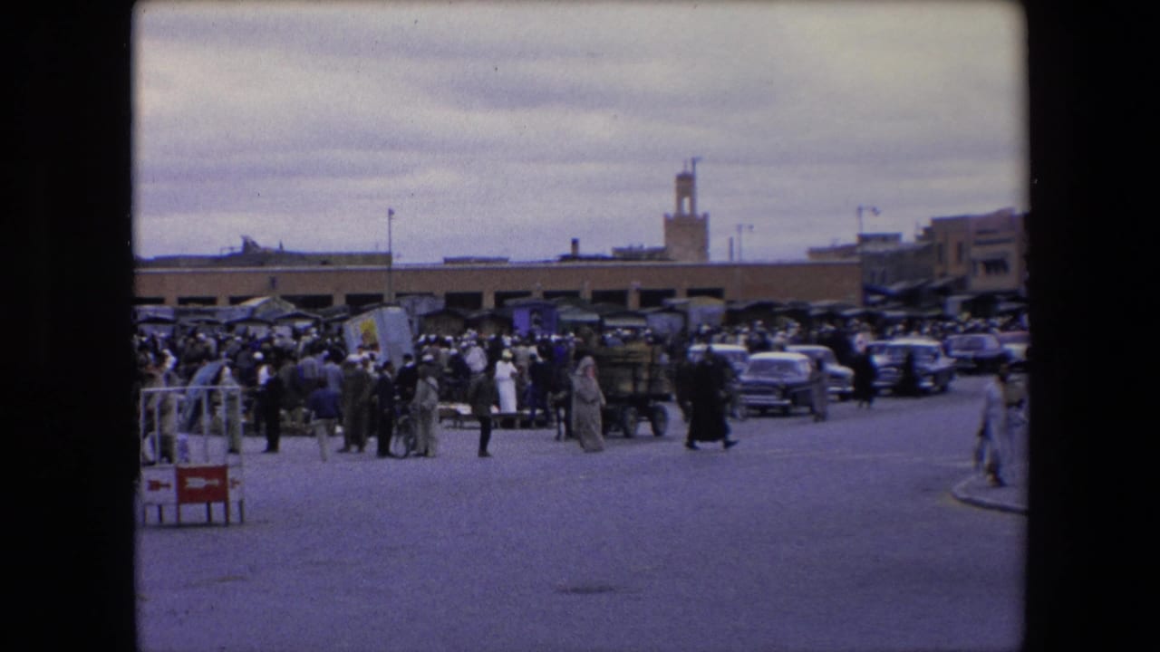 Market crowd with cars, carts, pedestrians, and a minaret visible above the buildings.