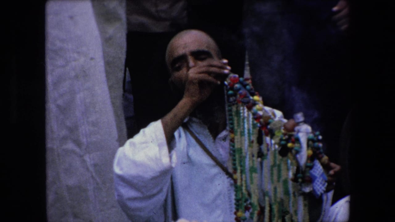 Seated man in a white robe smoking beside colorful bead strands.