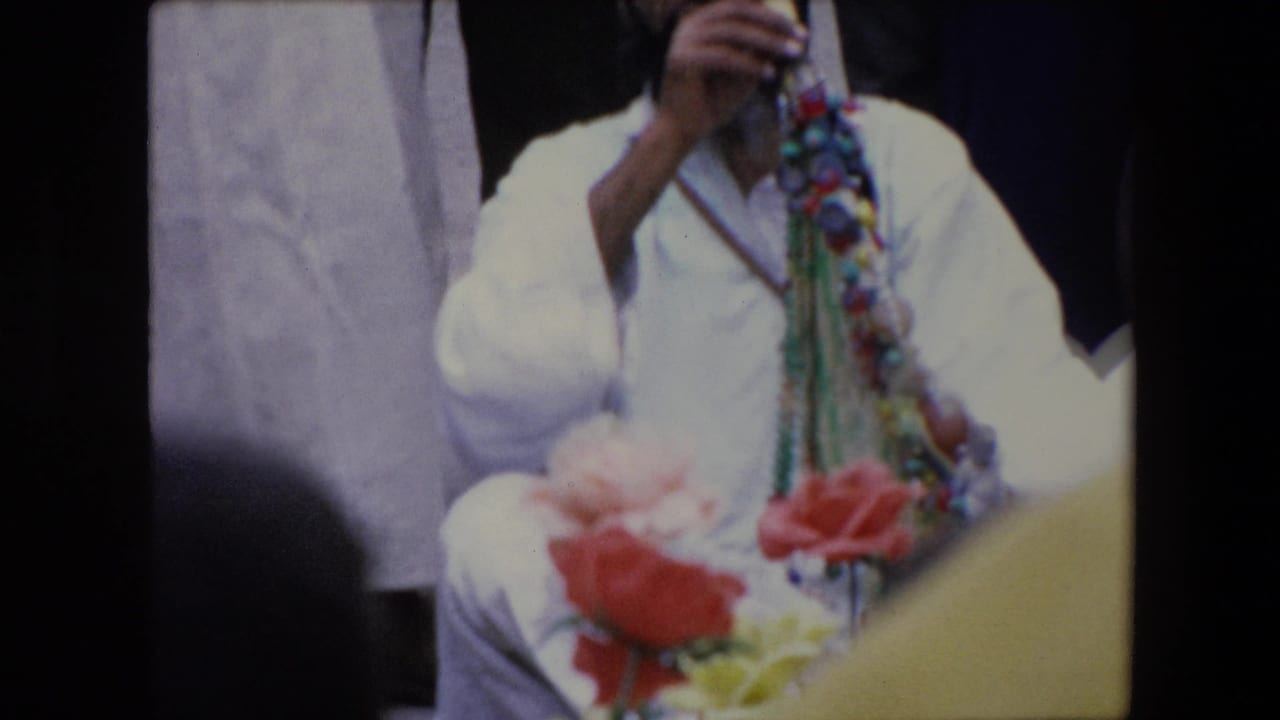 Robed figure with bead strands and flowers in the foreground.