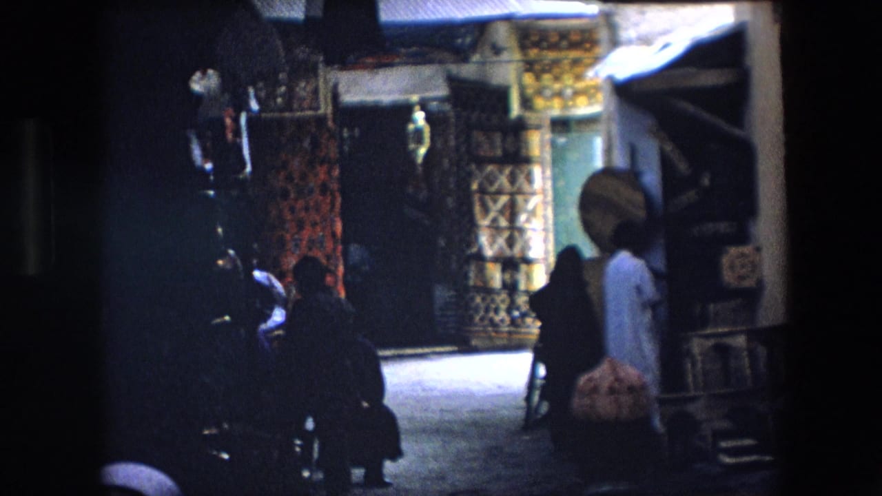 1971 Algeria 8mm frame showing pedestrians in a dim covered market alley lined with textiles and displayed goods.