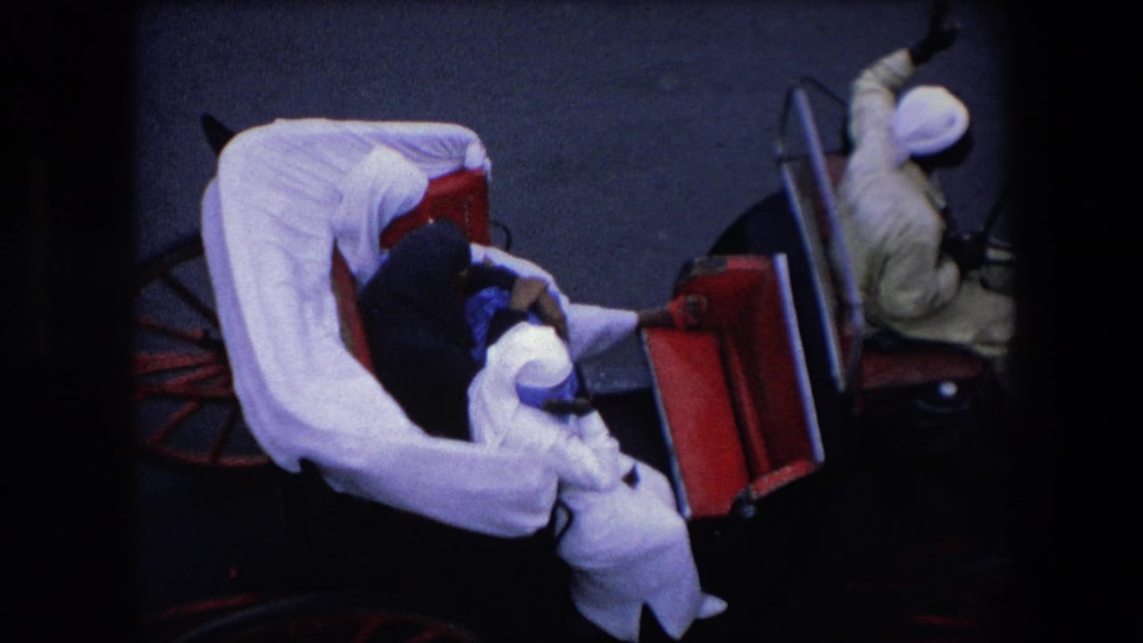 1971 Algeria home-movie frame showing an overhead view of a white-draped horse-drawn carriage with passengers in light and dark garments and a driver seated in front.