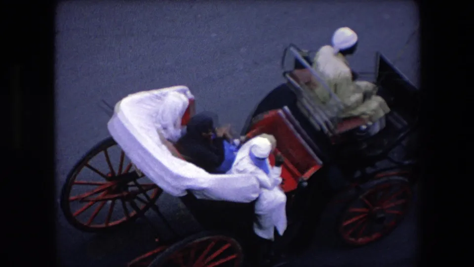 1971 Algeria frame showing the carriage from above, with passengers seated beneath white fabric, red carriage details, wooden wheels, and a driver in a light garment nearby.