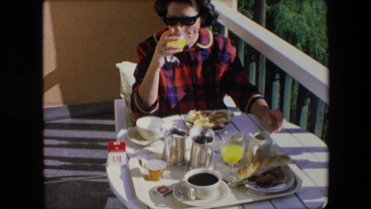Woman raises a glass of orange juice above a breakfast table on a sunny balcony.