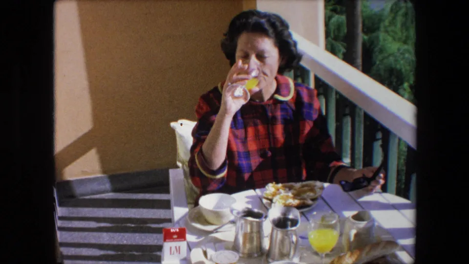 The 1971 Algeria frame shows the woman raising a glass of orange juice beside a breakfast plate, coffee service, tableware, and a balcony railing in bright patio light.