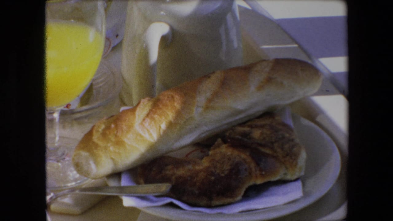 Bread and pastry on a white plate beside orange juice and a cream-colored pitcher.