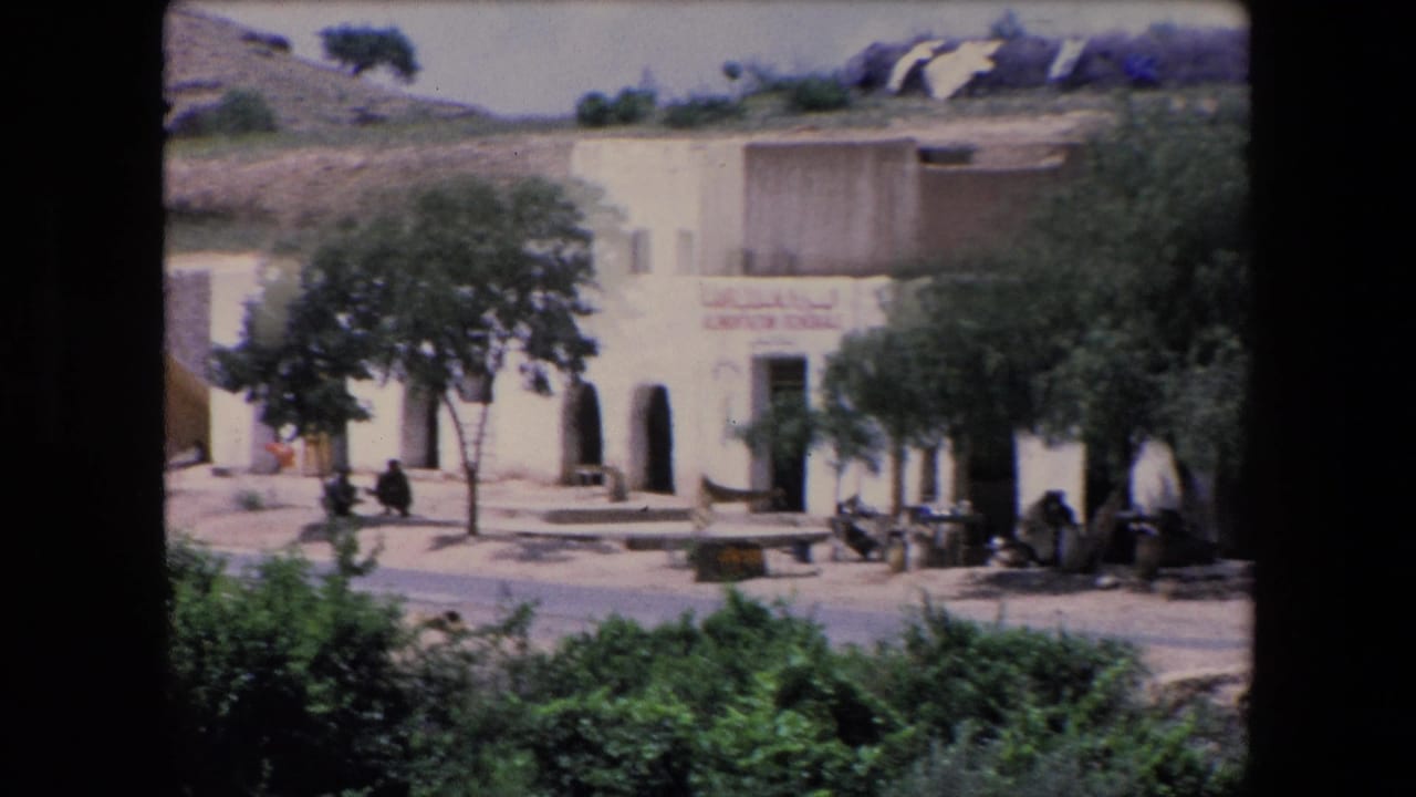 White general store building with trees, hillside, and people sitting near the entrance.
