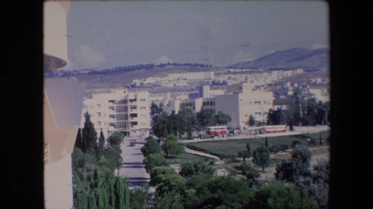 Elevated townscape with apartments, trees, road, and distant hills.