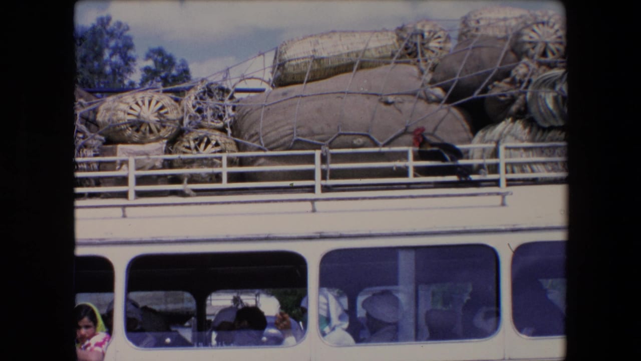 1971 Algeria home-movie frame showing a public bus loaded with sacks and woven baskets on the roof, with passengers visible through the side windows.